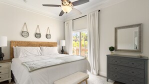 Ein Schlafzimmer mit einem großen Bett, Nachttischlampen, einem Deckenventilator, einem Schminktisch und einem Fenster mit Vorhängen.