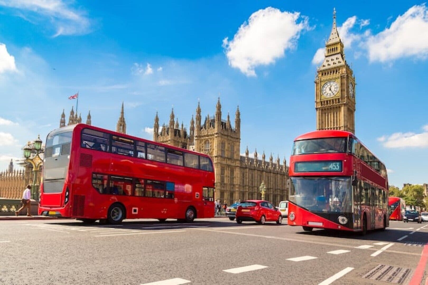 A red double-decker bus on a city street with a historic building and a clock tower in the background.