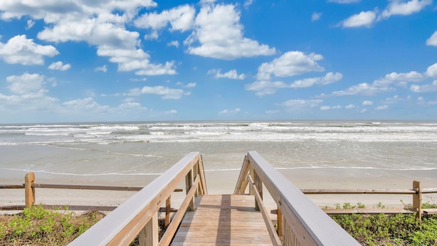 A wooden boardwalk leading to a beach with waves and a clear sky.
