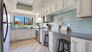 A modern kitchen with white cabinetry, a large window, and a view of the outdoors.