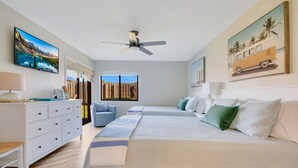 A bedroom with two beds, a ceiling fan, a TV, and a window with a view of mountains.