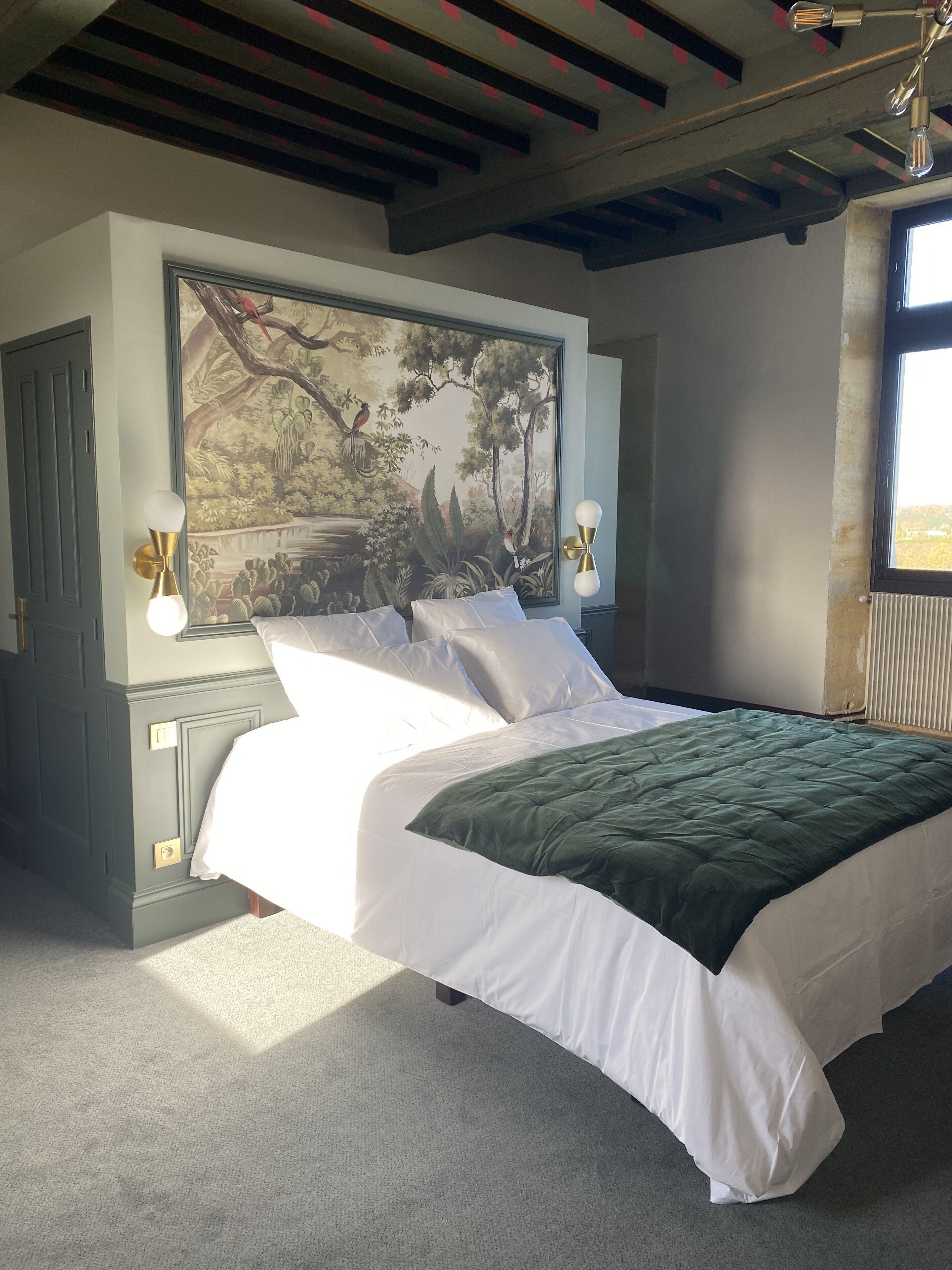 Une chambre avec un grand lit, un tableau au mur et une fenêtre donnant sur un beau paysage.