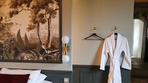 Ein Hotelzimmer mit einem Bett, einem Bademantel an einem Kleiderhaken, einem Baumgemälde und einer Lampe.