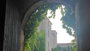 Ein rundbogenförmiger Durchgang führt zu einem Innenhof mit einem Kiesweg und einem Gebäude mit efeuüberwucherten Mauern.