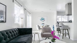 A modern living room with a dark sofa, a round coffee table with a vase of flowers, and a dining area with chairs and a table.