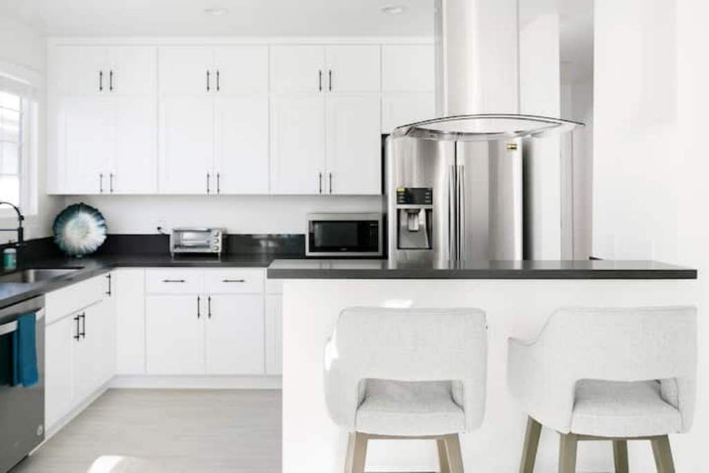 A modern kitchen with white cabinets, stainless steel appliances, and two bar stools.