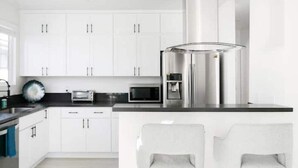 A modern kitchen with white cabinets, stainless steel appliances, and two bar stools.