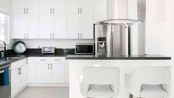 A modern kitchen with white cabinets, stainless steel appliances, and two bar stools.