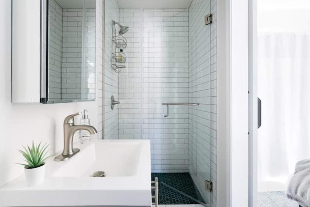 A modern bathroom with white subway tiles, a white sink with a single faucet, a small potted plant, and a shower area with a glass door.