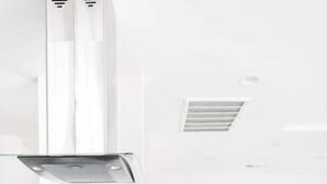 A modern kitchen with a built-in stove, a grey upholstered bar stool, and a flat-screen TV mounted on the wall.