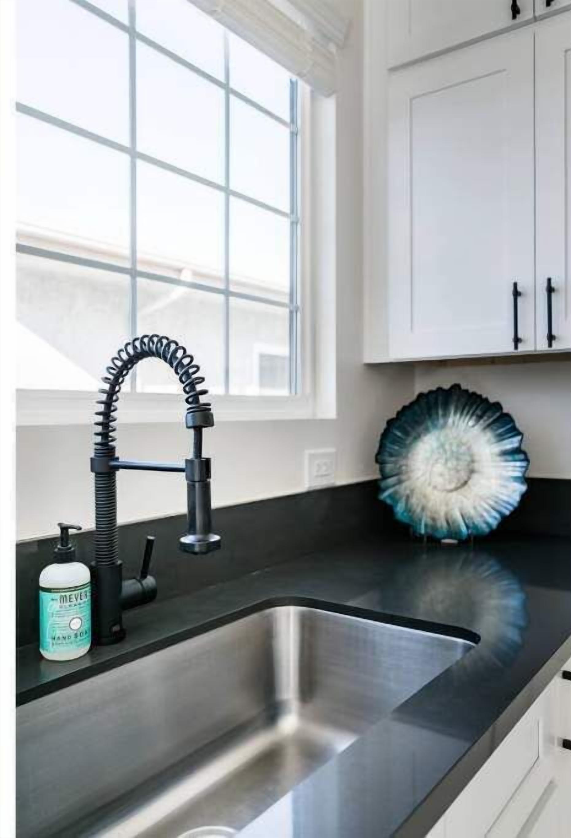 A modern kitchen with a stainless steel sink, a black faucet, and a decorative blue and white plate on the counter.