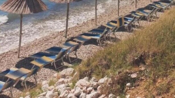 A beach with lounge chairs and thatched umbrellas, rocky hills in the background, and a clear blue sea. - Modern apartment Oleandra, 5 only 250 meters from the sea (Baska)