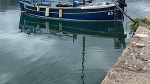 A harbor with a blue boat docked, calm water, and a mountainous backdrop. - Modern apartment Oleandra, 5 only 250 meters from the sea (Baska)