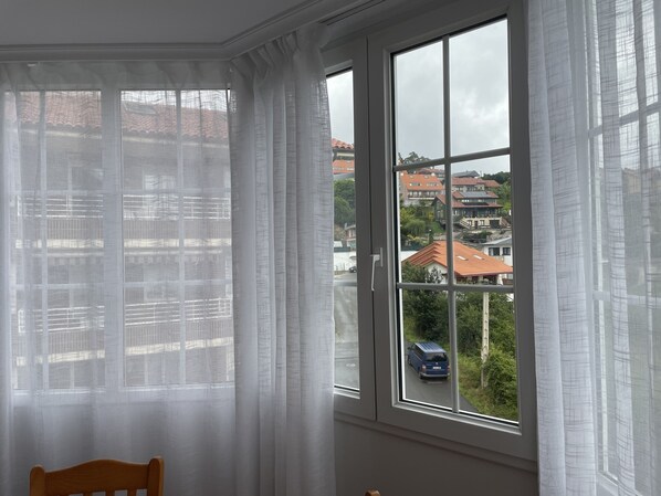 A room with a large window, white curtains, and a wooden chair.