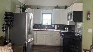 Una cocina compacta con armarios blancos, un refrigerador de acero inoxidable y una estufa negra.