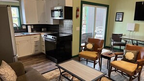 Un espacio habitable compacto con kitchenette, un sofá, dos sillones y una mesa de centro.