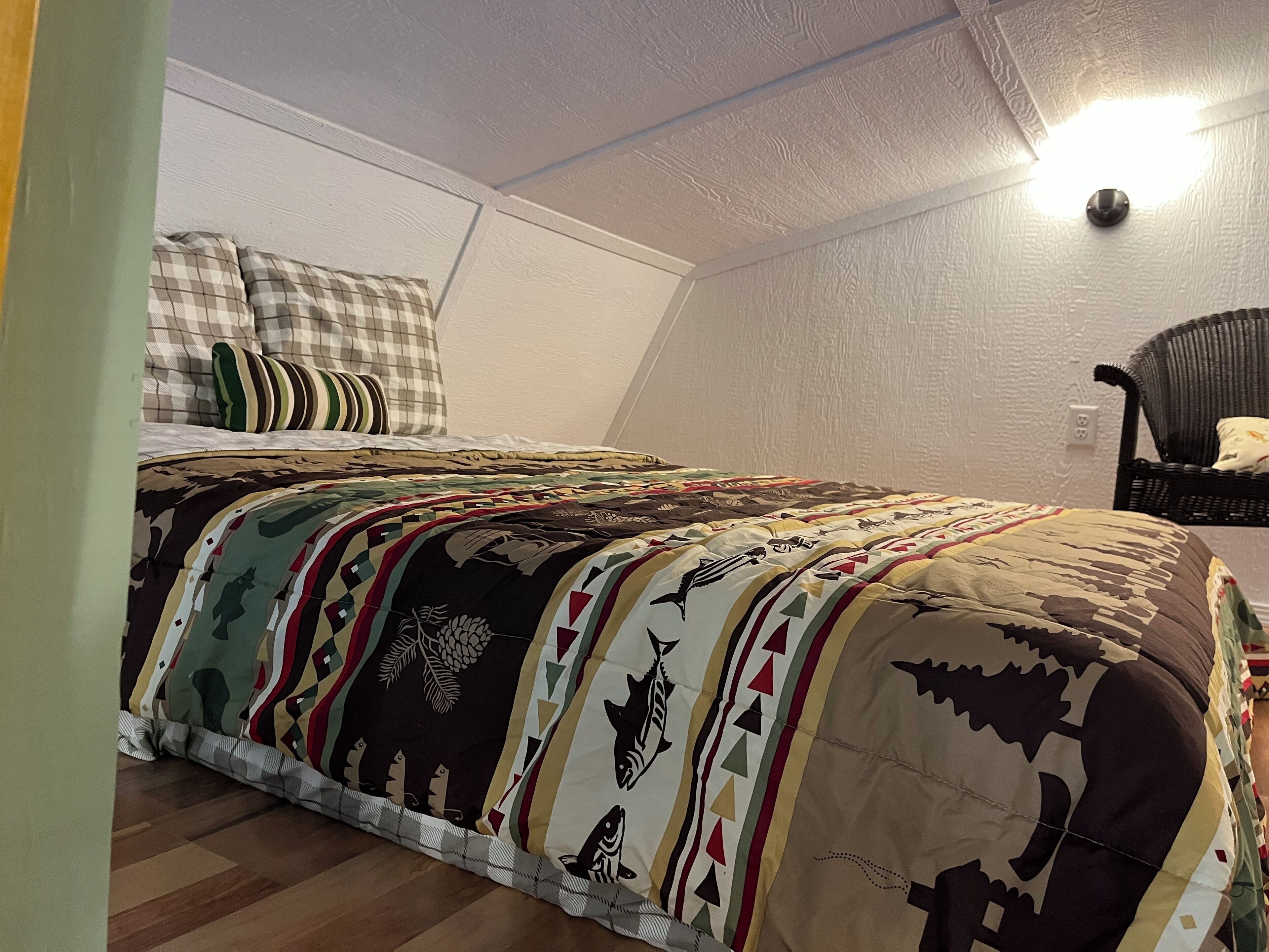Een slaapkamer met een bed bekleed met een gebreide deken, een stoel en een wandlamp.