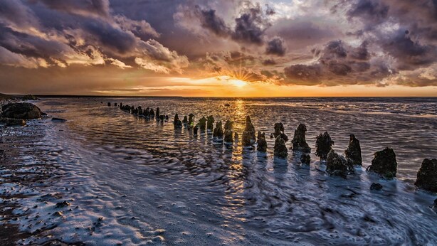 Een zonsondergang boven een strand met rotsformaties in het water.