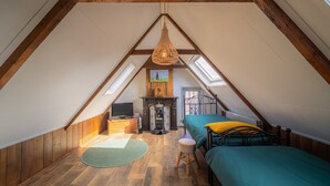 Een gezellige slaapkamer onder het dak met houten balken, een hanglamp, een bed, een klein krukje, een radiator en een televisie.