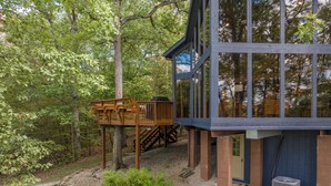 A modern cabin with a wooden deck and a glass-enclosed upper level, surrounded by dense forest. - A Shore Thing by Innsbrook Vacations! (Innsbrook)