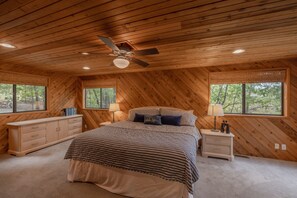 A bedroom with a wooden ceiling, a bed with a striped bedspread, two bedside tables with lamps, and large windows offering a view of trees. - A Shore Thing by Innsbrook Vacations! (Innsbrook)