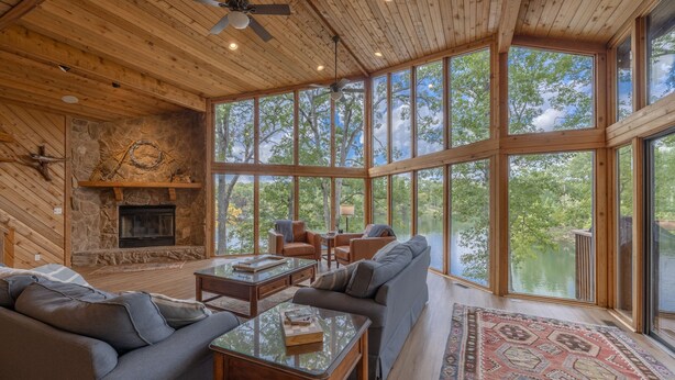 A spacious living room with a fireplace, large windows, and a view of a lake. - A Shore Thing by Innsbrook Vacations! (Innsbrook)