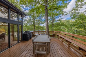 A wooden deck with a table and benches, surrounded by trees and a glass enclosure. - A Shore Thing by Innsbrook Vacations! (Innsbrook)