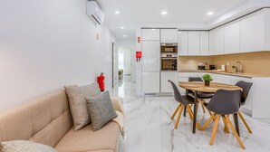 A modern kitchen with white cabinets, a dining area with a round table and chairs, and a beige sofa with cushions. - Sublime and Bright 2 BDR Apartment by LovelyStay (Quarteira)