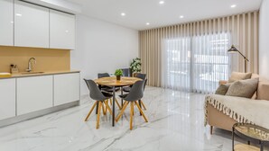 A modern living room with a sofa, a coffee table, and a dining area with a table and chairs. - Sublime and Bright 2 BDR Apartment by LovelyStay (Quarteira)