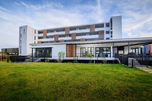 A modern multi-story building with a flat roof, large windows, and a covered outdoor area.