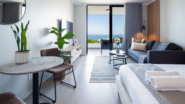 Ein modernes Hotelzimmer mit Balkon, einer Couch, einem Esstisch und einem Fernseher.