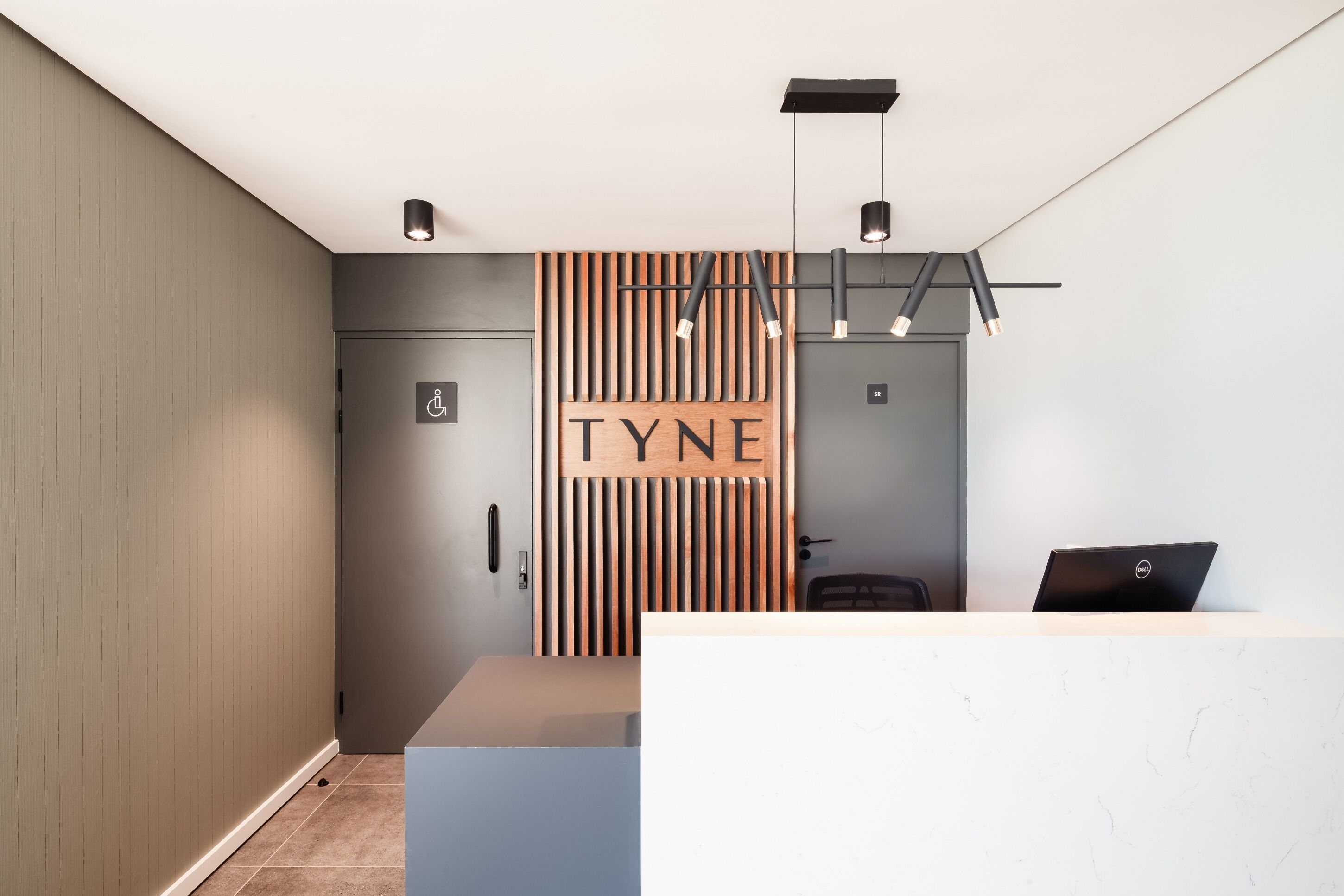 A reception area with a modern design, featuring a wooden slat wall with the name "TYNE" and a Dell laptop on the counter.