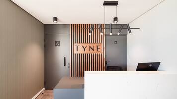 A reception area with a modern design, featuring a wooden slat wall with the name "TYNE" and a Dell laptop on the counter.