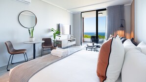 Ein modernes Hotelzimmer mit einem großen Bett, einem Schreibtisch, einem Sessel, einem kleinen Tisch und Meerblick.