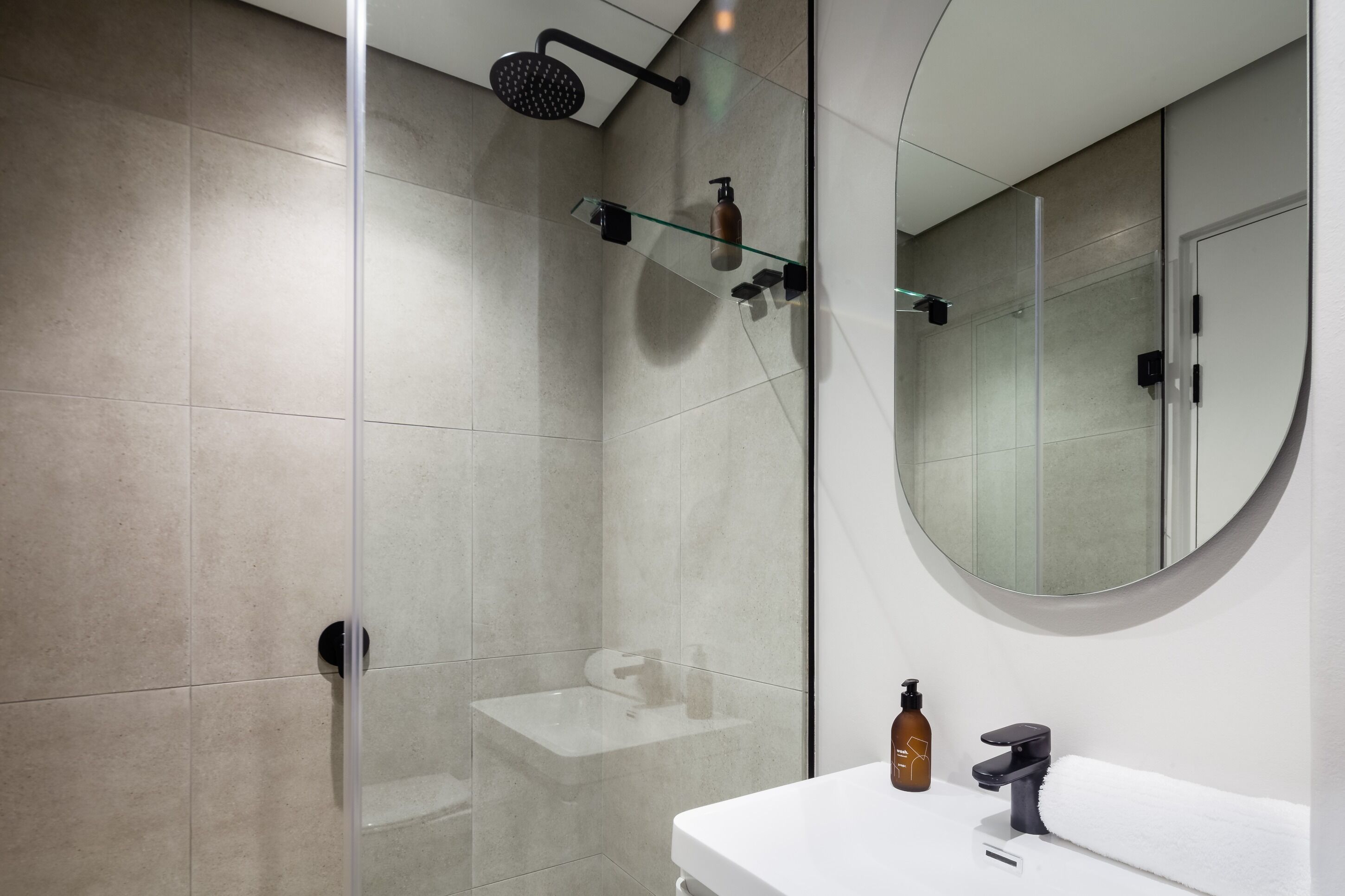 A modern bathroom with a glass shower enclosure, a white sink, and a round mirror.