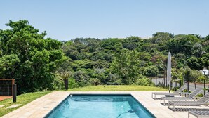Piscina retangular com borda azulejada, rodeada por um deck pavimentado.