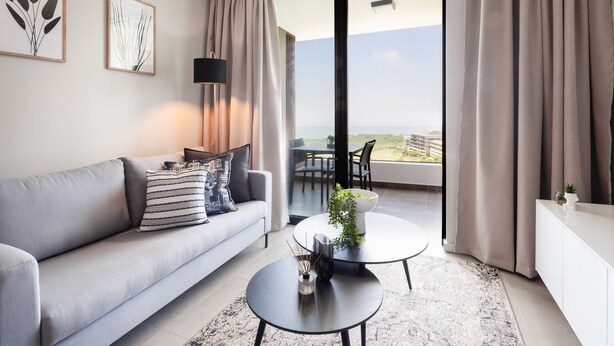 Sala de estar moderna com um sofá cinza, uma mesa de centro redonda e vista para o exterior por grandes portas deslizantes.
