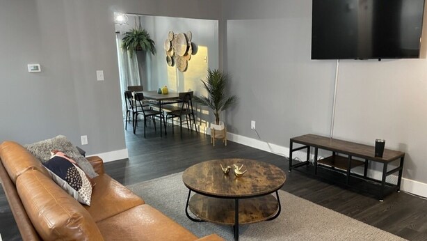 Een moderne woonkamer met een leren bank, een ronde salontafel en een flatscreen televisie aan de muur.