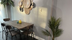 Een eetgedeelte met een houten tafel en stoelen, een geweven kunstwerk aan de muur en een potplant.