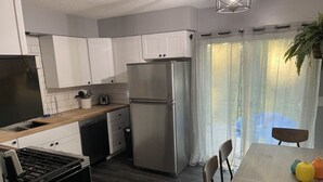 Een moderne keuken met witte kasten, een roestvrijstalen koelkast, een gasfornuis en een eettafel met stoelen.