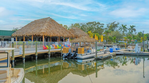 A waterfront area with thatched-roof structures, a dock with colorful chairs, and a marina with boats. - ALL-NEW Waterfront with Balcony, Pool, Tiki Bar, Gym (Sarasota)