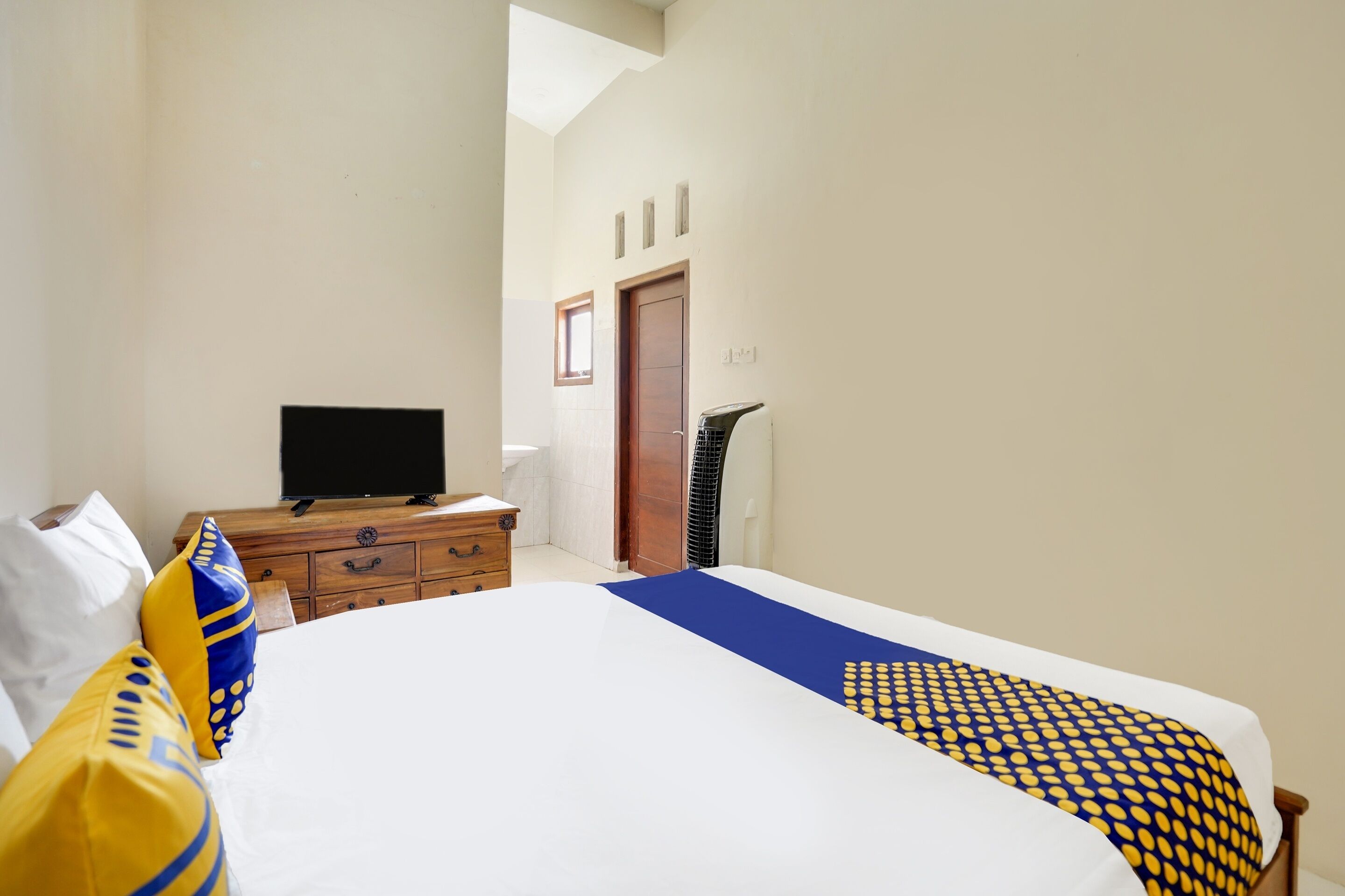 A hotel room with a bed, a television on a wooden dresser, and a window.