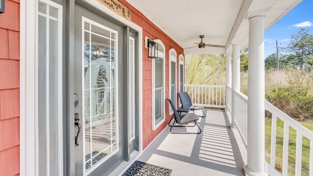 Un porche couvert à l’extérieur rouge, avec des balustrades blanches et une chaise noire.