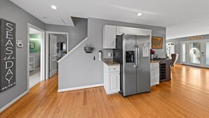 Une cuisine moderne avec des meubles gris, un réfrigérateur en acier inoxydable et un plancher en bois.