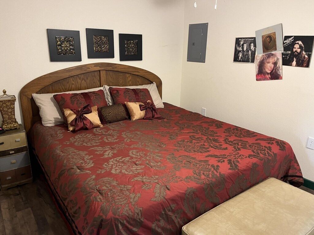 Un dormitorio con una cama grande, cabecera de madera y un banco. Hay tres cuadros enmarcados en la pared.
