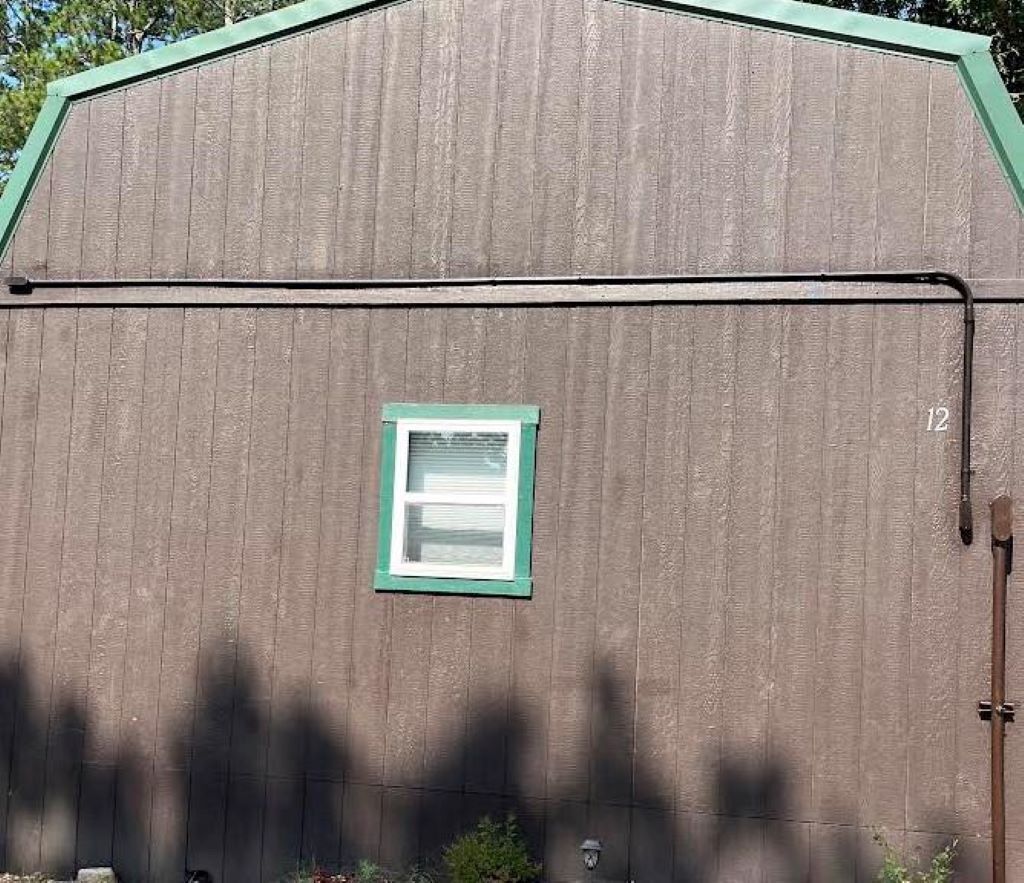 Un abri en bois avec un toit vert, une petite fenêtre et une porte.