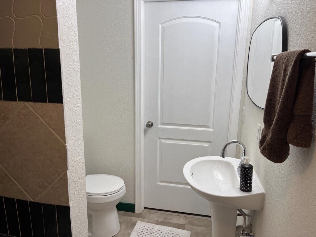 Un baño con inodoro y lavamanos blancos, y una toalla colgada en un perchero.