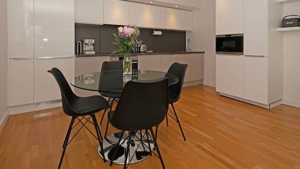 A modern kitchen with white cabinets, a black dining table with four chairs, and a microwave. - Penthouse Kew (Brentford)
