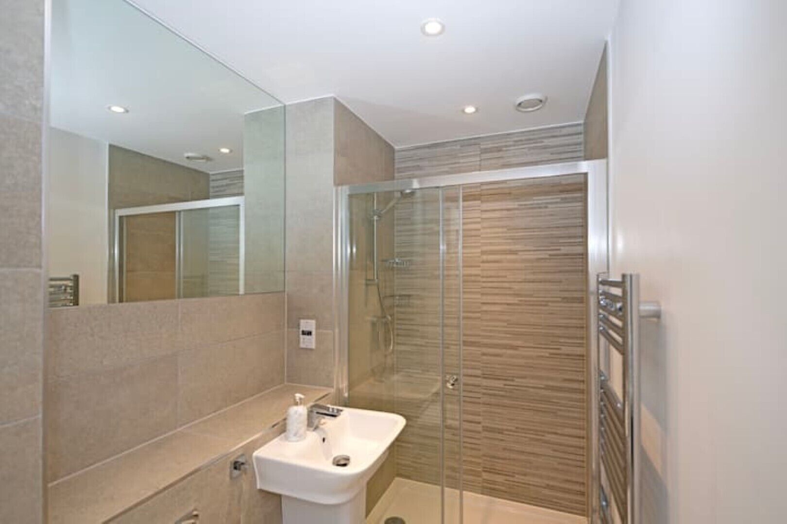 Een moderne badkamer met een douchecabine van glas, een witte wastafel en een grote spiegel.