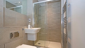 A modern bathroom with a glass shower enclosure, a pedestal sink, and a toilet. - Penthouse Kew (Brentford)
